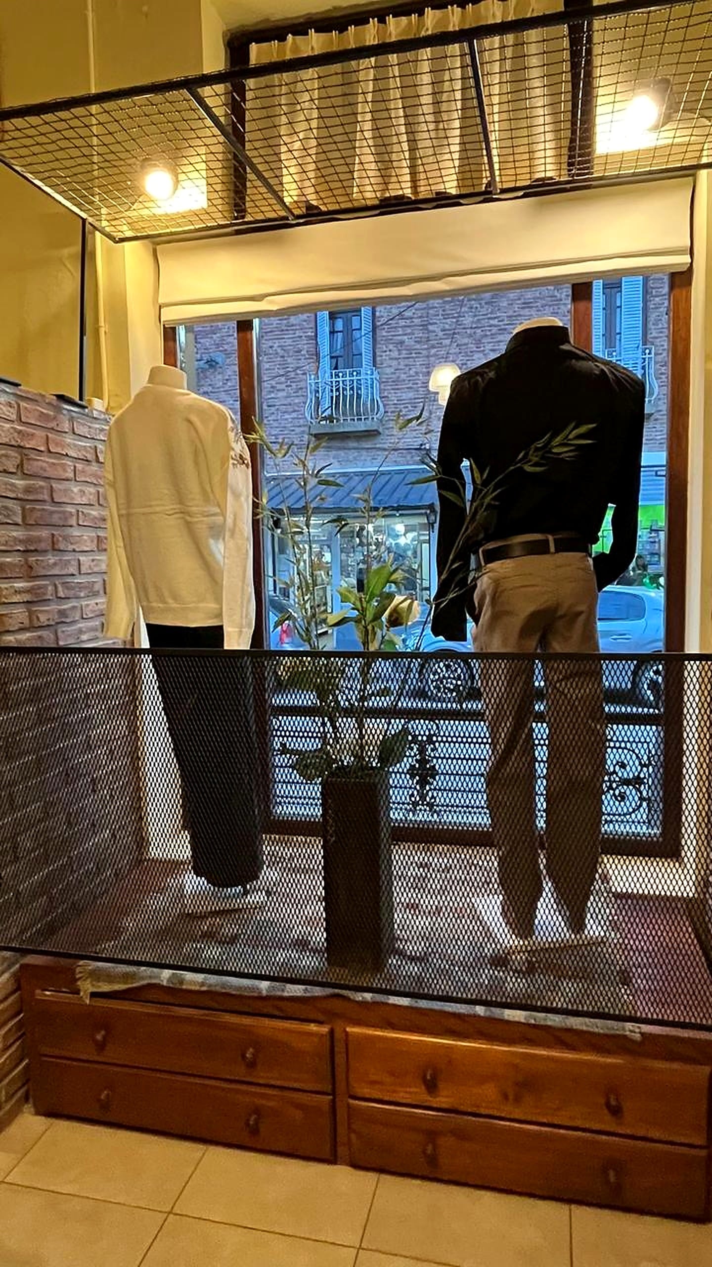 Vidriera interior con ropa de hombre: una camisa clara y una camisa oscura con pantalones en maniquíes.