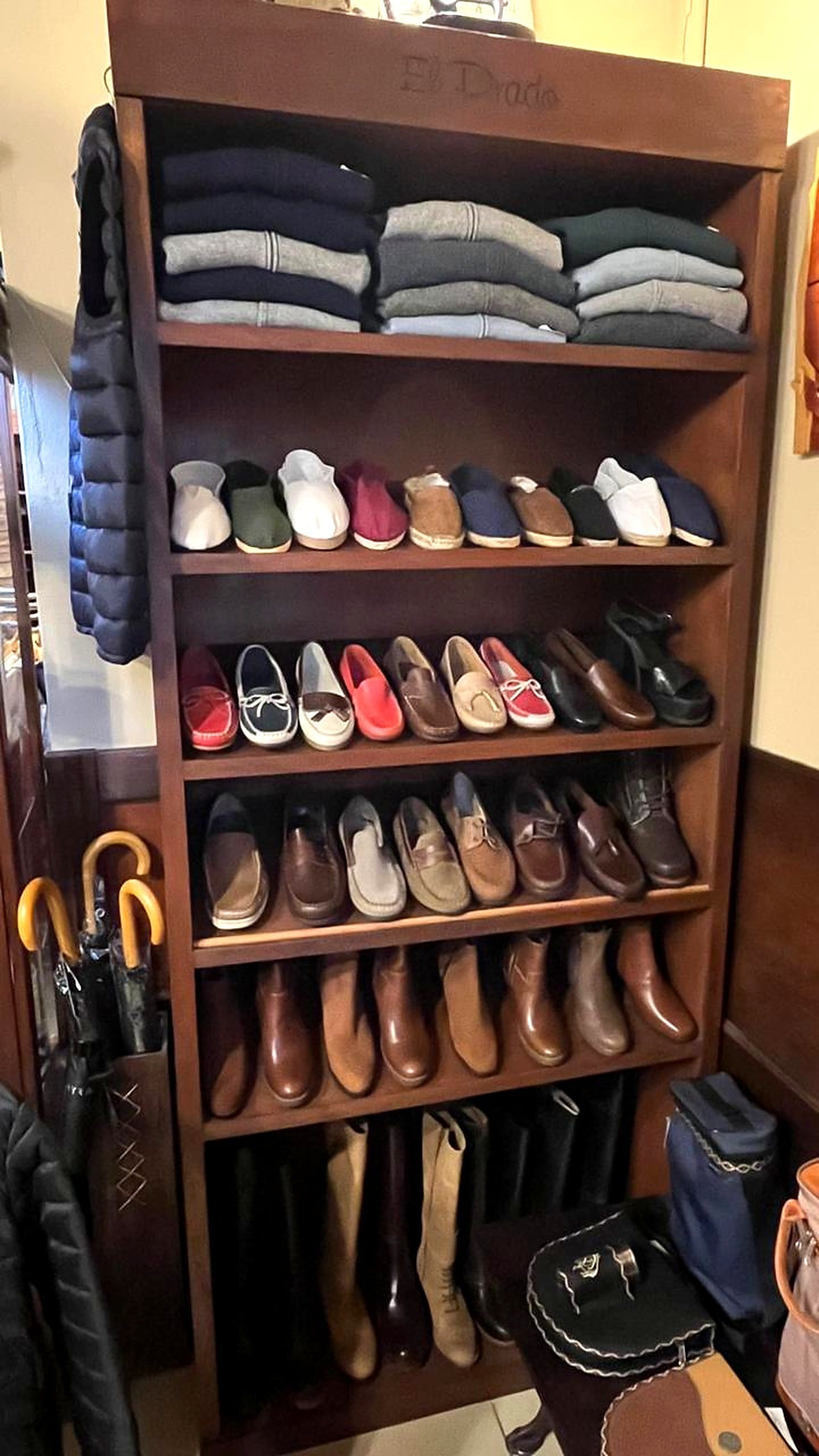 Estantería de madera con alpargatas de colores, náuticos, mocasines y botas, y pulóveres doblados arriba.