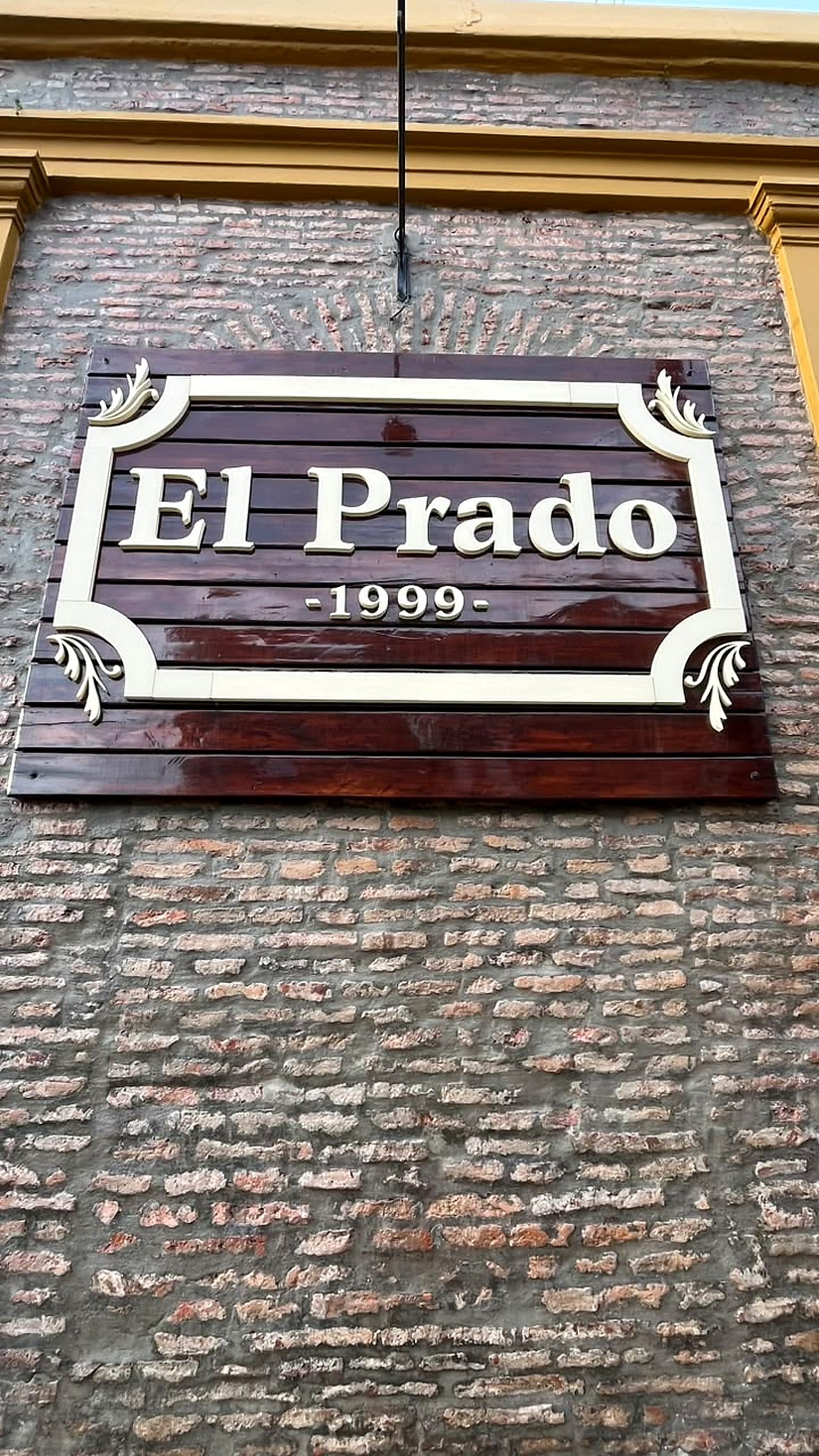 Cartel de madera de El Prado, 1999, sobre la pared de ladrillo del local.